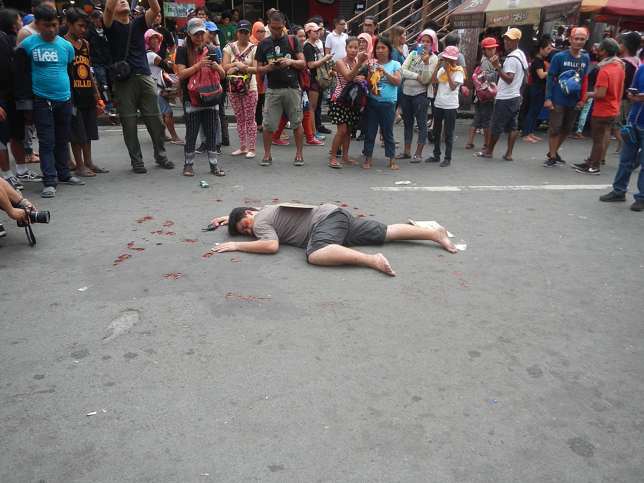 Demonstrator reenacts what the (alleged) extrajudicial killing looked like. Writing on the cardboard placed on the body was typically used in the crime allegedly related to drugs since Rodrigo Duterte was inaugurated as the president.